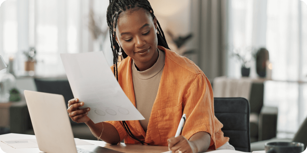 A woman in front of a computer holding a piece of paper and writing something down