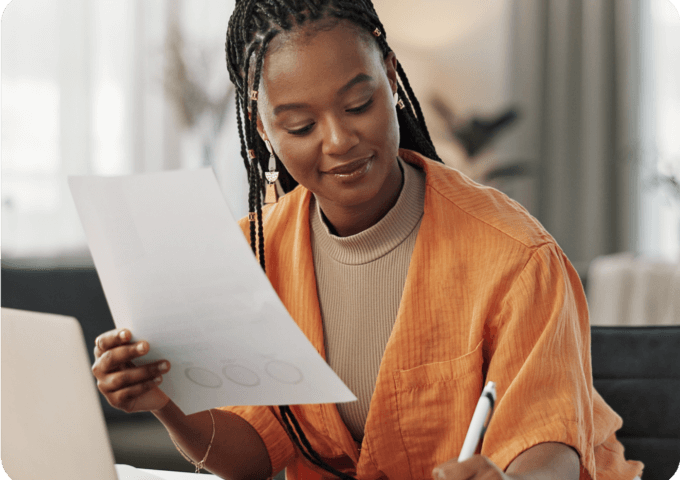 A woman in front of a computer holding a piece of paper and writing something down