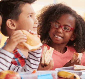 young children smiling and eating lunch at school